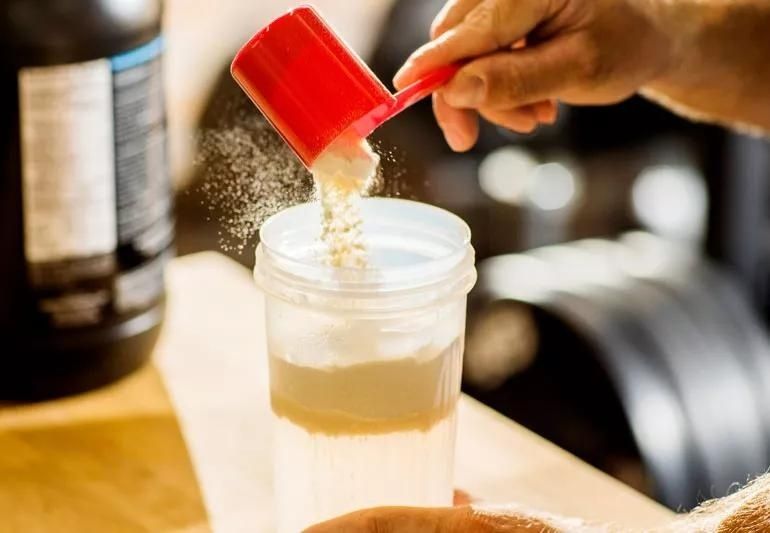 Rött mått häller proteinpulver i en shaker med vätska